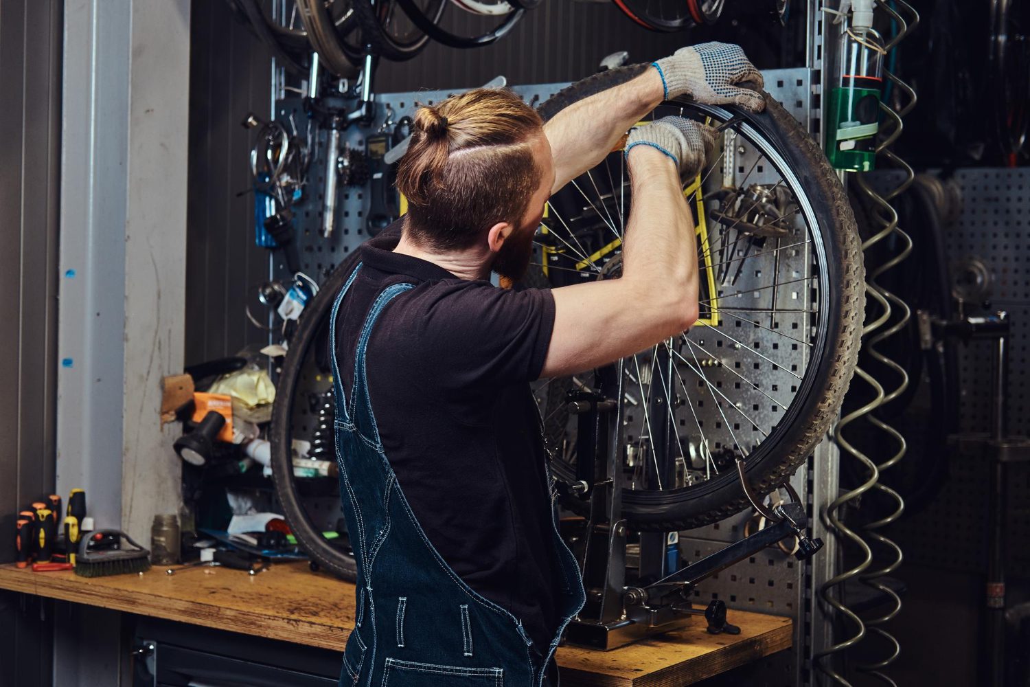 handsome redhead male jeans coverall working with bicycle wheel repair shop worker removes bicycle tire workshop